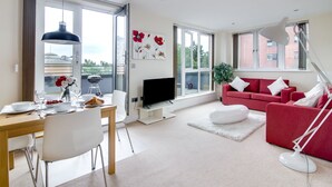 Uma sala de estar moderna com um sofá vermelho, uma televisão de tela plana e um espaço de jantar com uma mesa posta para dois.