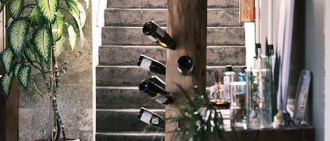 Una escalera con un poste de madera que sostiene botellas de vino, una planta en maceta y una mesa con diversos objetos.