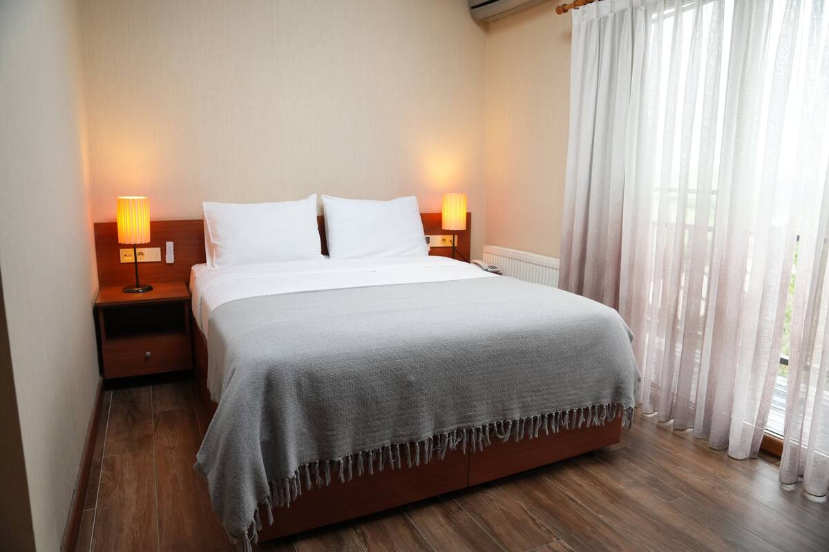 A neatly made bed with a grey blanket, wooden headboard, and two bedside lamps.