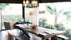 A dining area with a wooden table and benches, a chandelier, and a view of greenery outside. - Cevizdibi Otel (Kartepe)