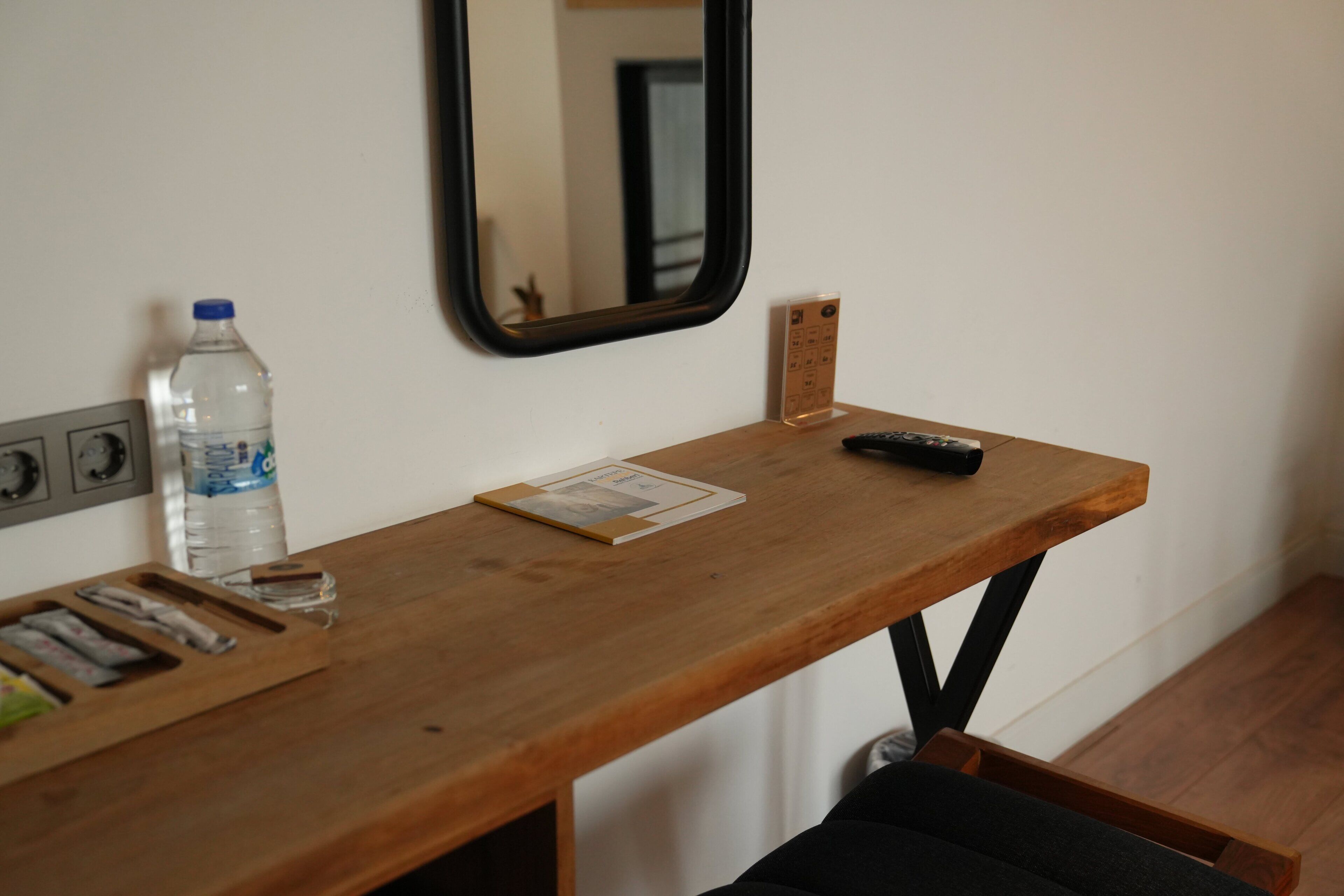 A wooden desk with a water bottle, remote control, and a small card.
