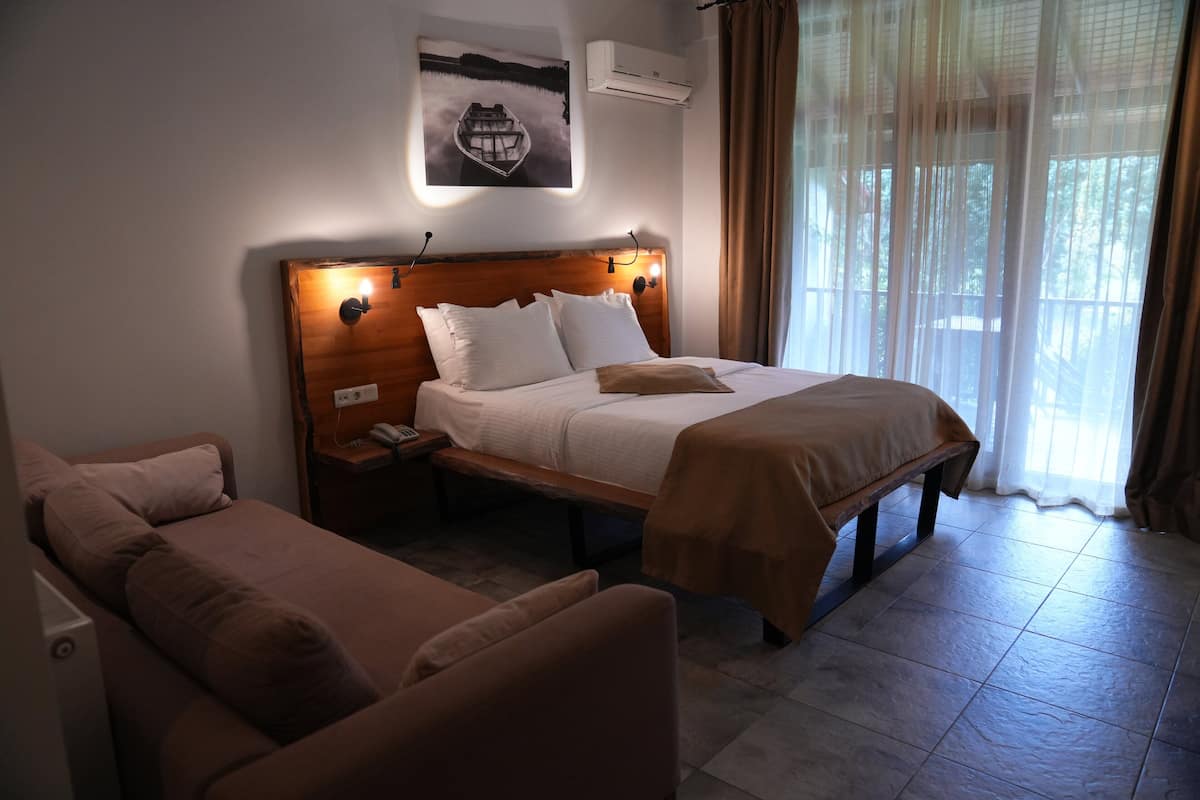 A hotel room with a large bed, a bedside table with a lamp, a bench, and a view of a lake through sheer curtains.