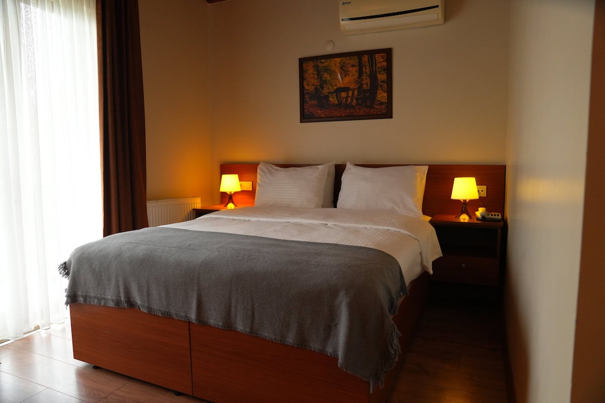 A neatly made bed with a grey blanket, two bedside lamps, and a painting on the wall.