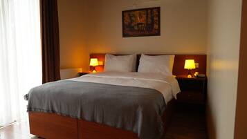 A neatly made bed with a grey blanket, two bedside lamps, and a painting on the wall.