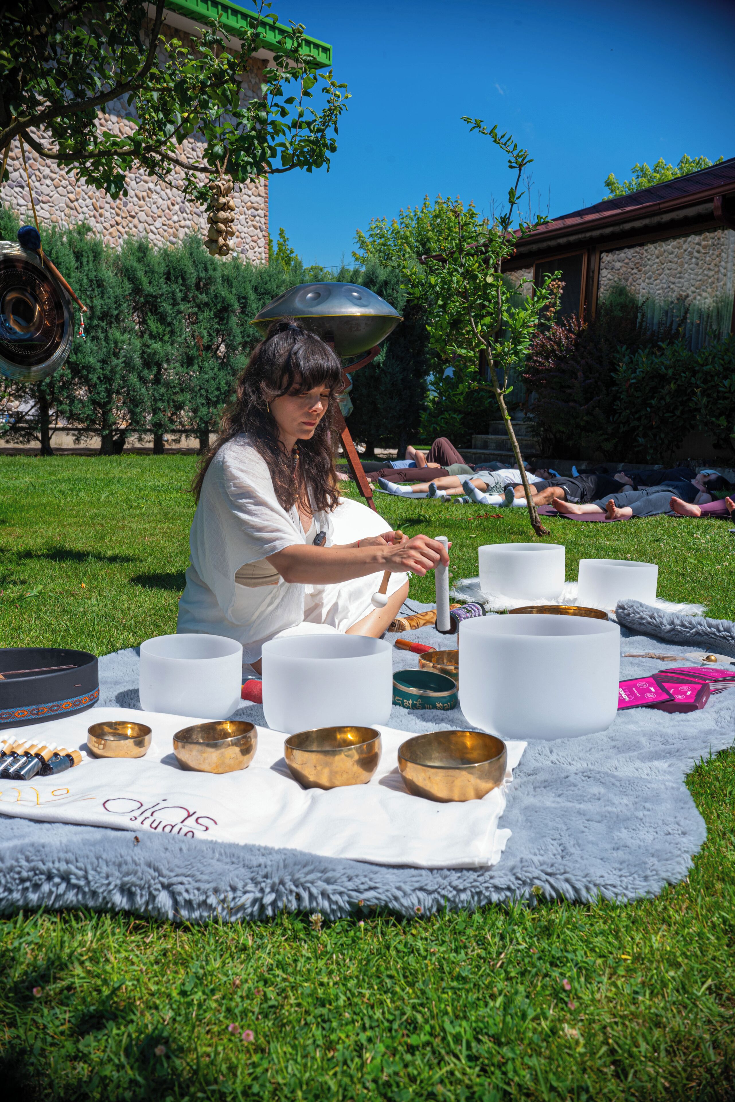 Una persona sentada sobre una manta al aire libre, con cuencos de meditación y un gong.