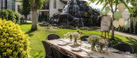 An outdoor dining area with a waterfall backdrop, neatly set tables, and a sign for a birthday celebration.