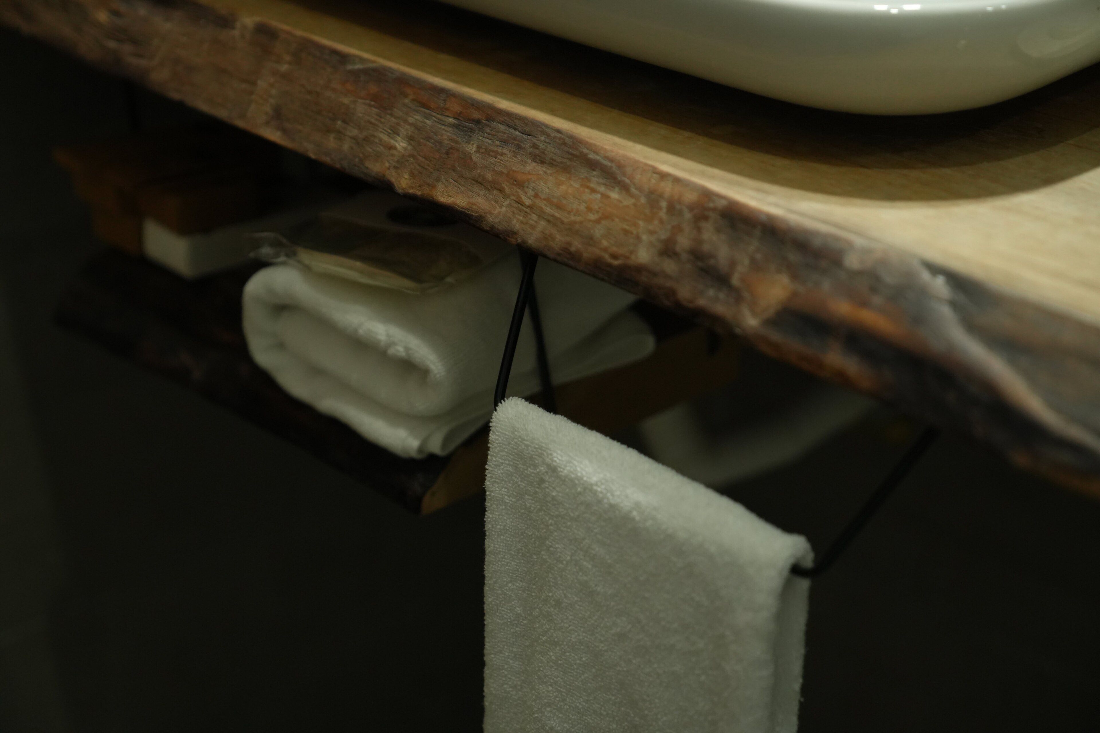 A wooden countertop with a white ceramic bowl and a folded white towel hanging below.
