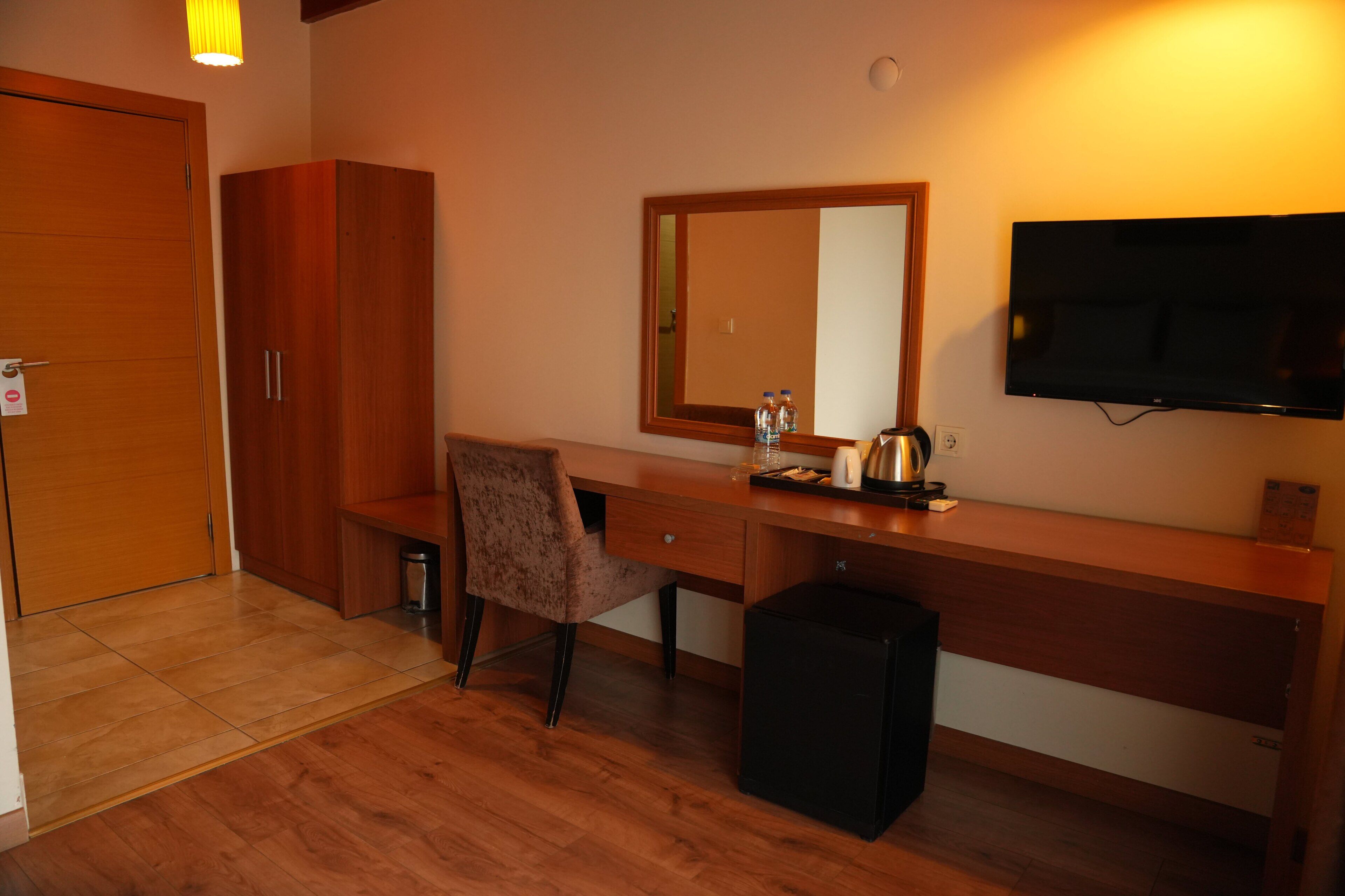 Une chambre d’hôtel avec un bureau en bois, une chaise, une petite poubelle noire, un téléviseur et un miroir au mur.