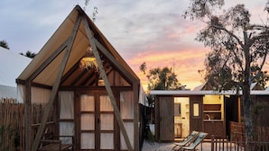 Una cabaña de madera con techo triangular, un porche con banca y una pequeña zona de estar al aire libre.