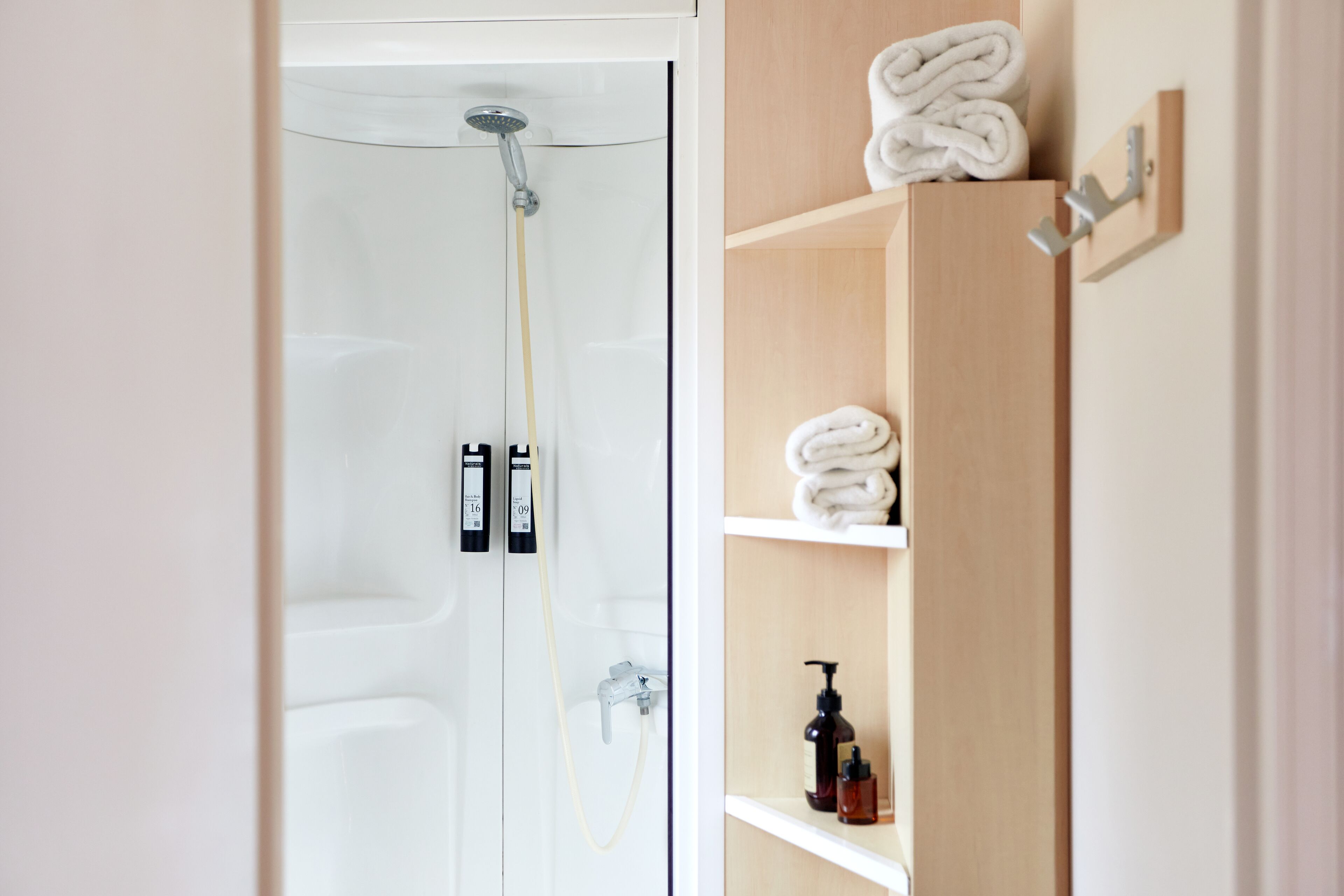 A bathroom with a shower, a towel rack, and shelves with toiletries.