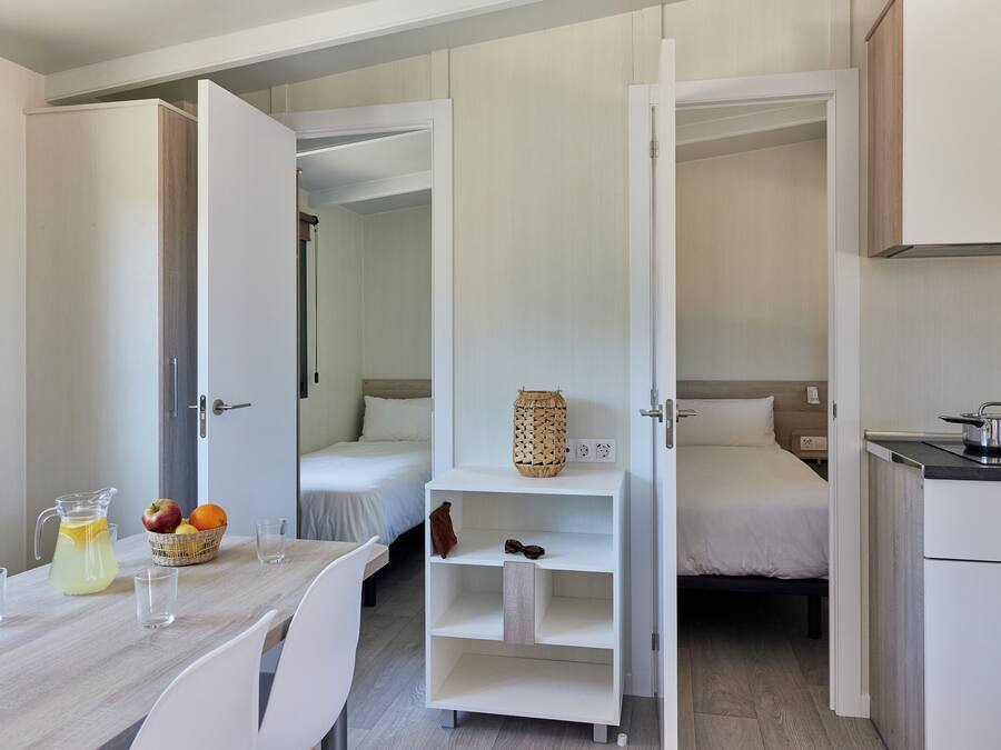 A compact hotel room with a kitchenette, a dining area with a table and chairs, and a bed with a nightstand.