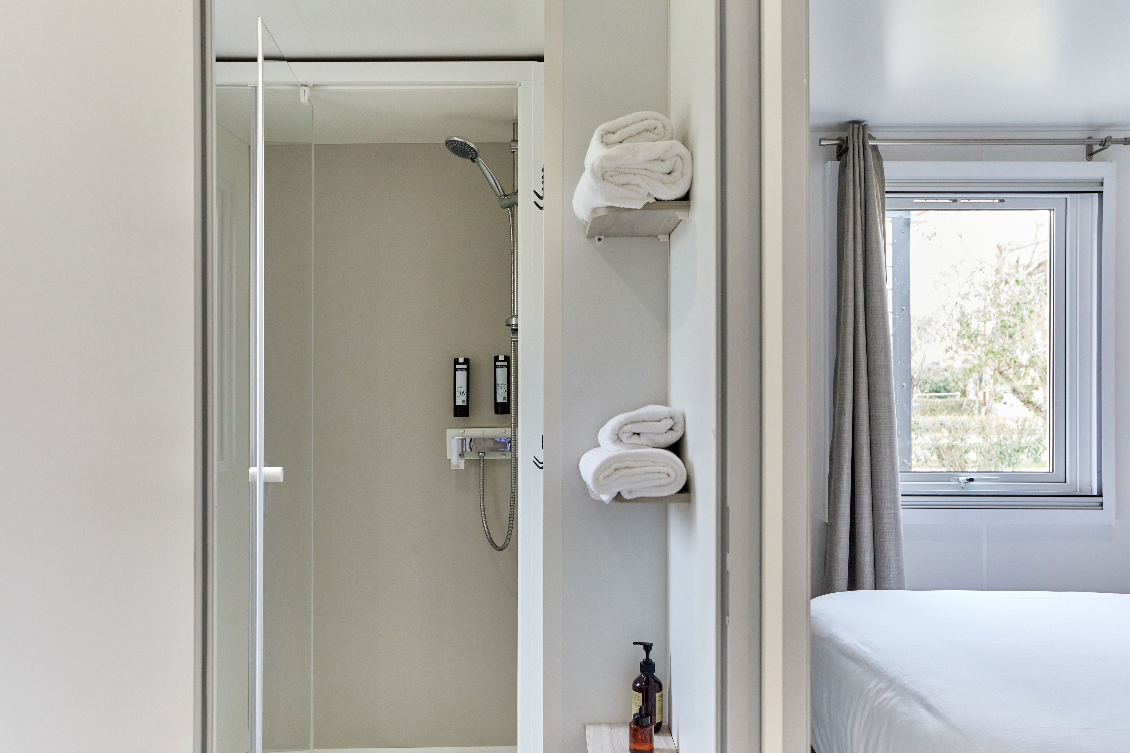 Une salle de bain moderne avec une porte de douche en verre, des toilettes et un porte-serviettes où sont soigneusement pliées les serviettes.