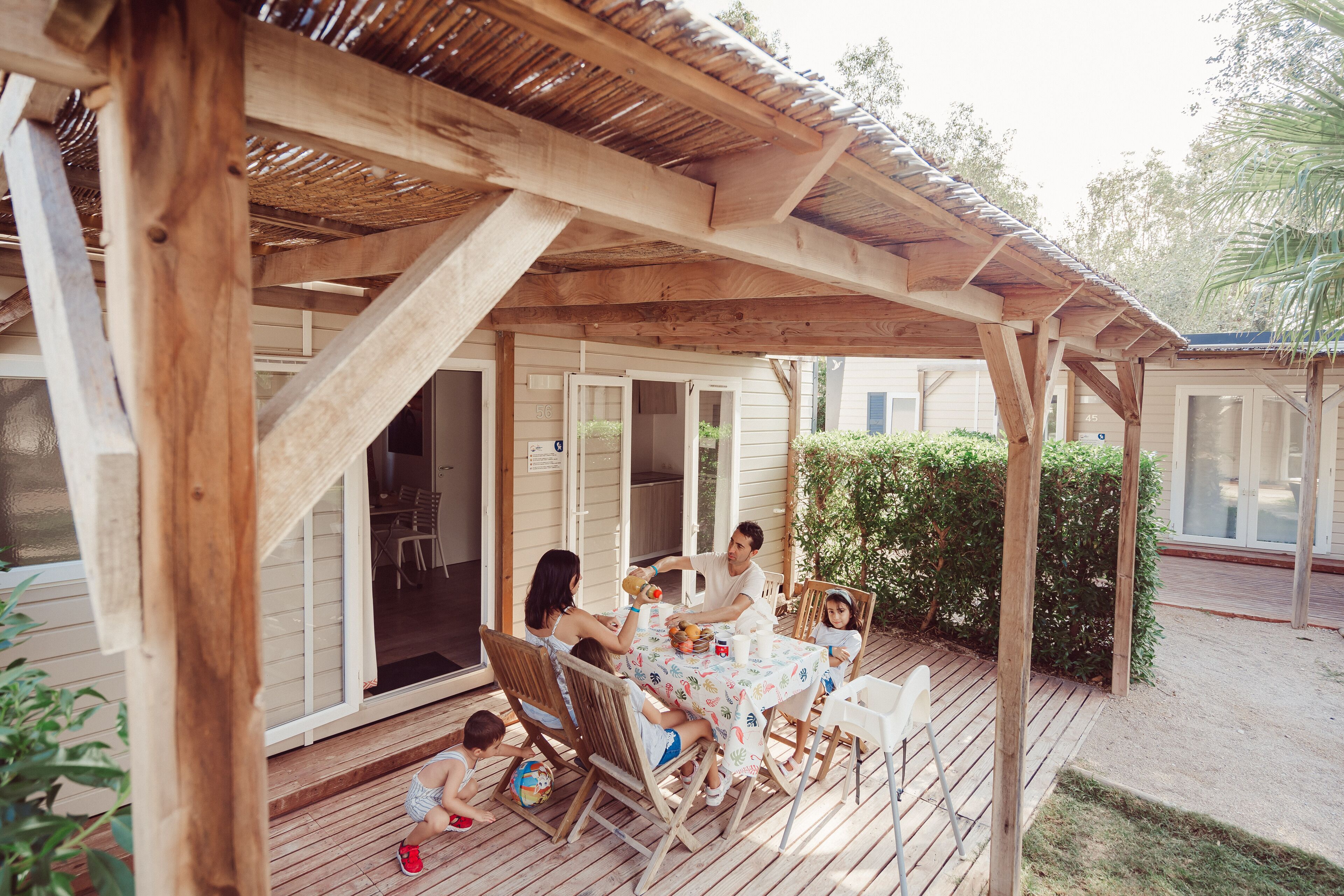 Une terrasse en bois avec un espace patio couvert, des sièges d’extérieur et une vue sur une maison en arrière-plan.