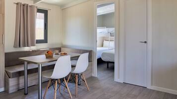 Una habitación compacta con kitchenette, una zona de comedor con dos sillas, un banco y una cama con literas.