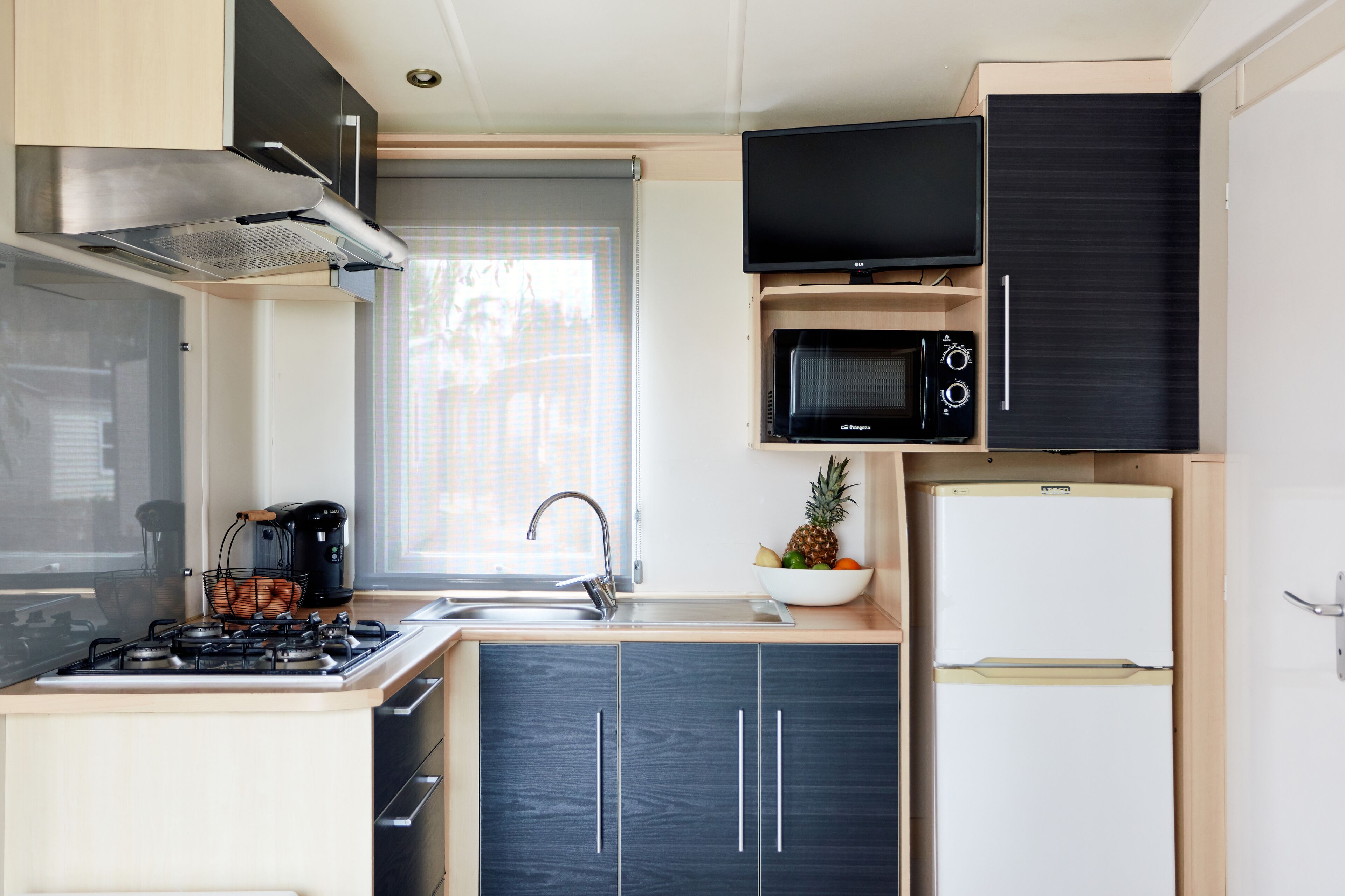 Une cuisine de taille réduite équipée d’une cuisinière à gaz, d’un évier, d’un four à micro-ondes et d’un petit réfrigérateur.