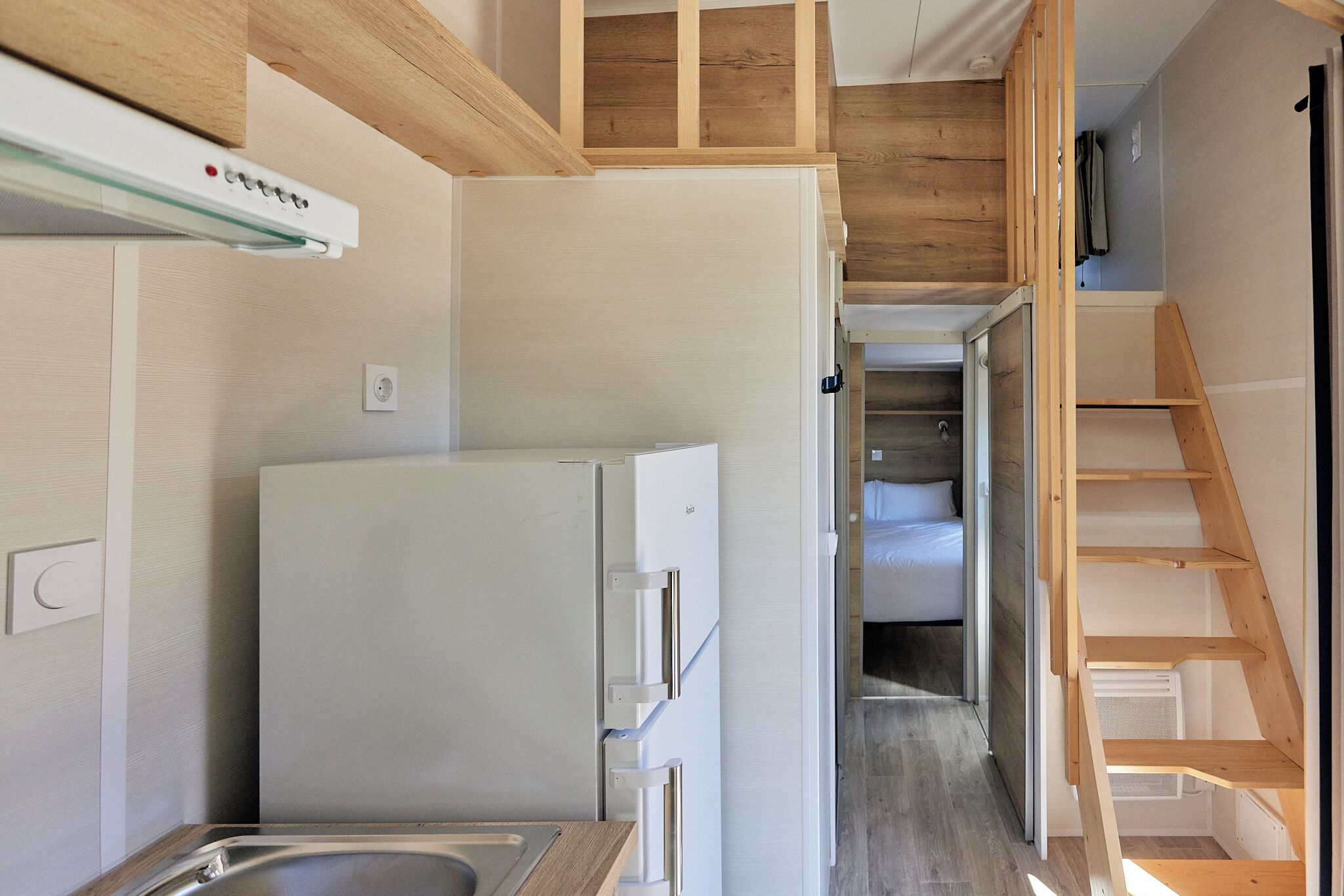 Una cocina compacta con refrigerador integrado, muebles de madera y un lavamanos pequeño.