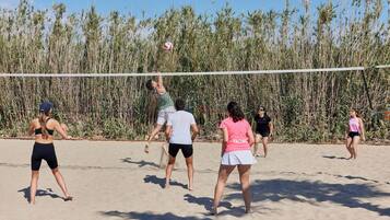 Un grupo de personas juega al voleibol en una playa arenosa con hierba alta al fondo.