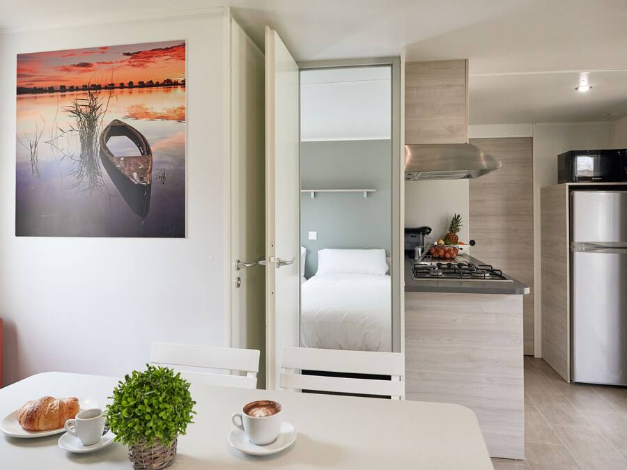 Habitación de hotel compacta con comedor, kitchenette y cama visible a través de una puerta abierta.