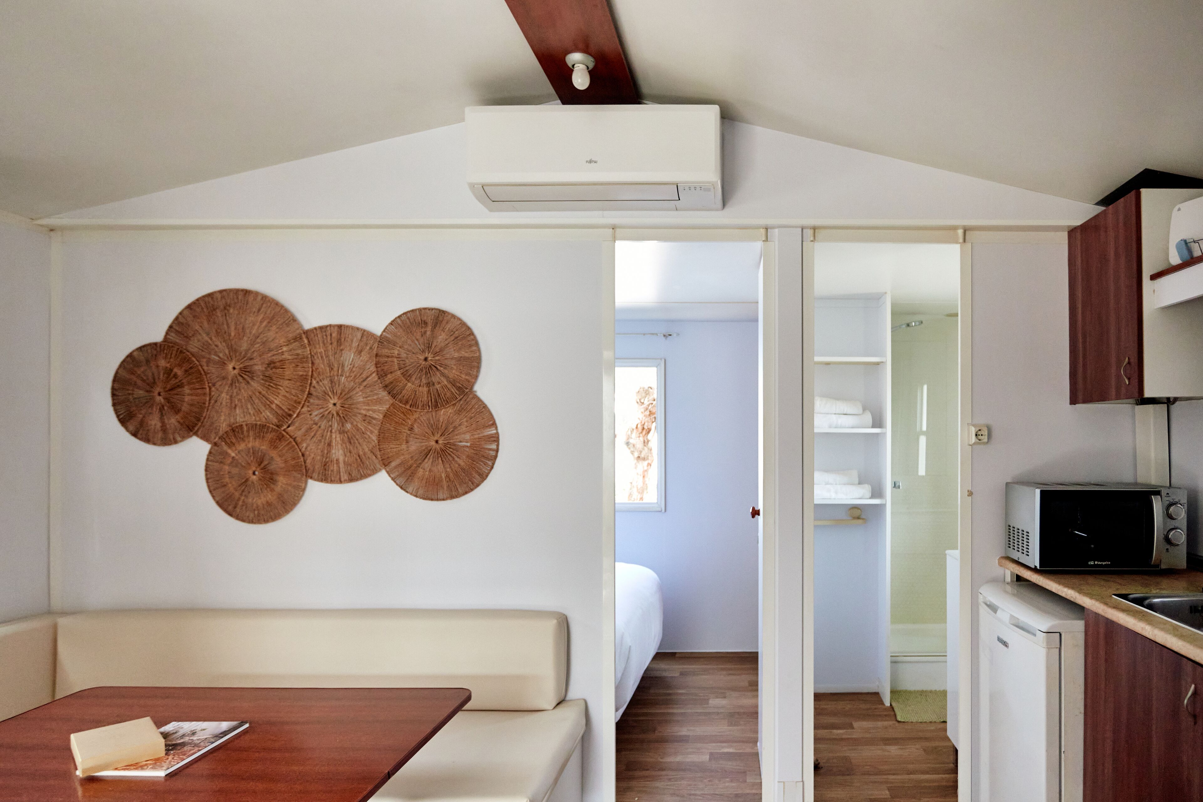 A compact living space with a kitchenette, a dining area with a wooden table, and a bed in the background.