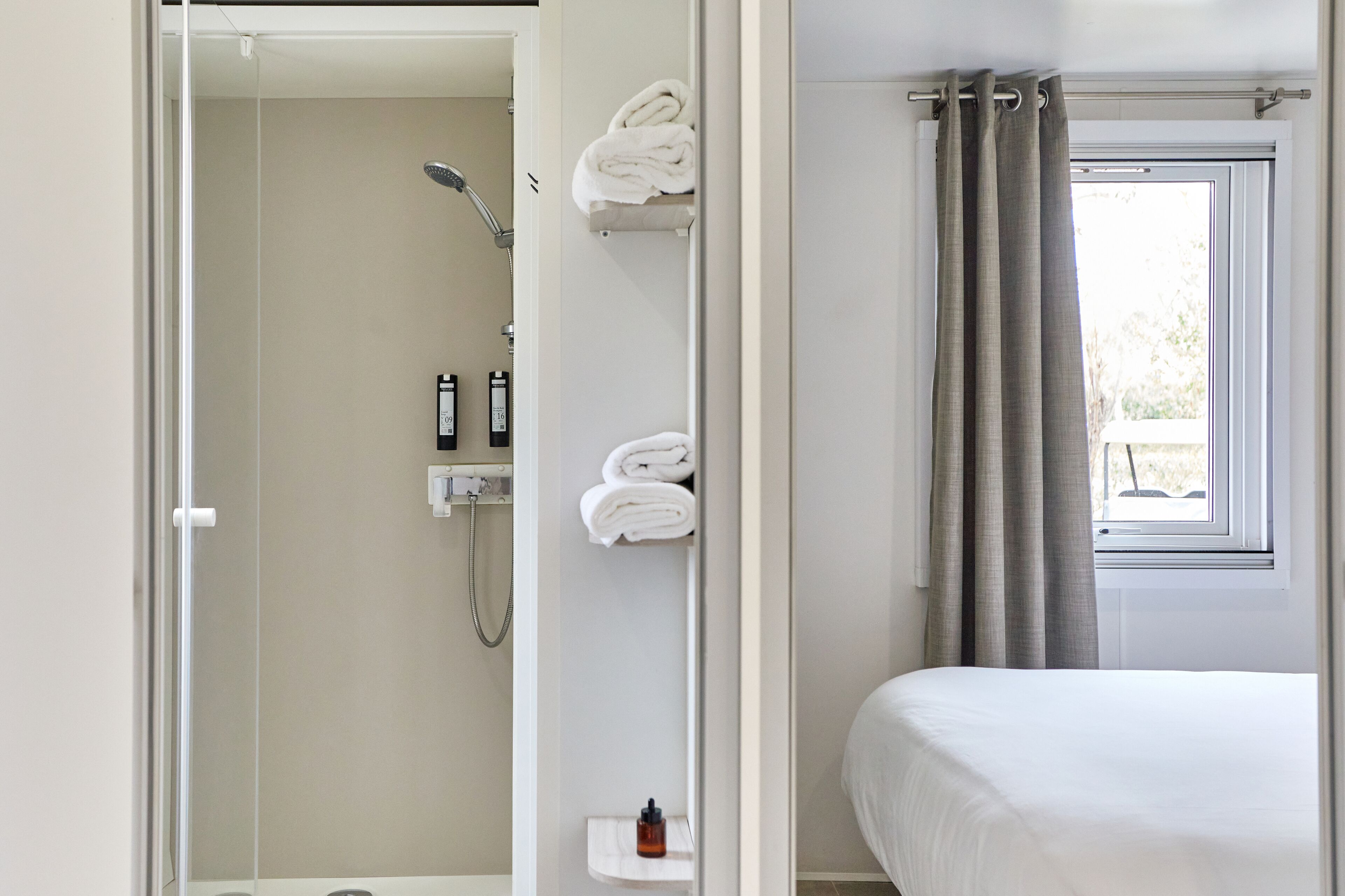A hotel room with a shower, a bed, and a window with curtains.