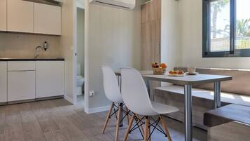 Een moderne keuken met witte kasten, een eethoek met een tafel en stoelen, en een raam met uitzicht op palmbomen.