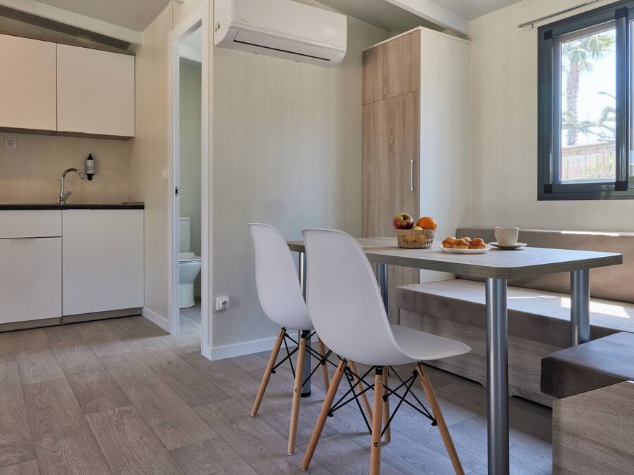 Een moderne keuken met witte kasten, een eethoek met een tafel en stoelen, en een raam met uitzicht op palmbomen.