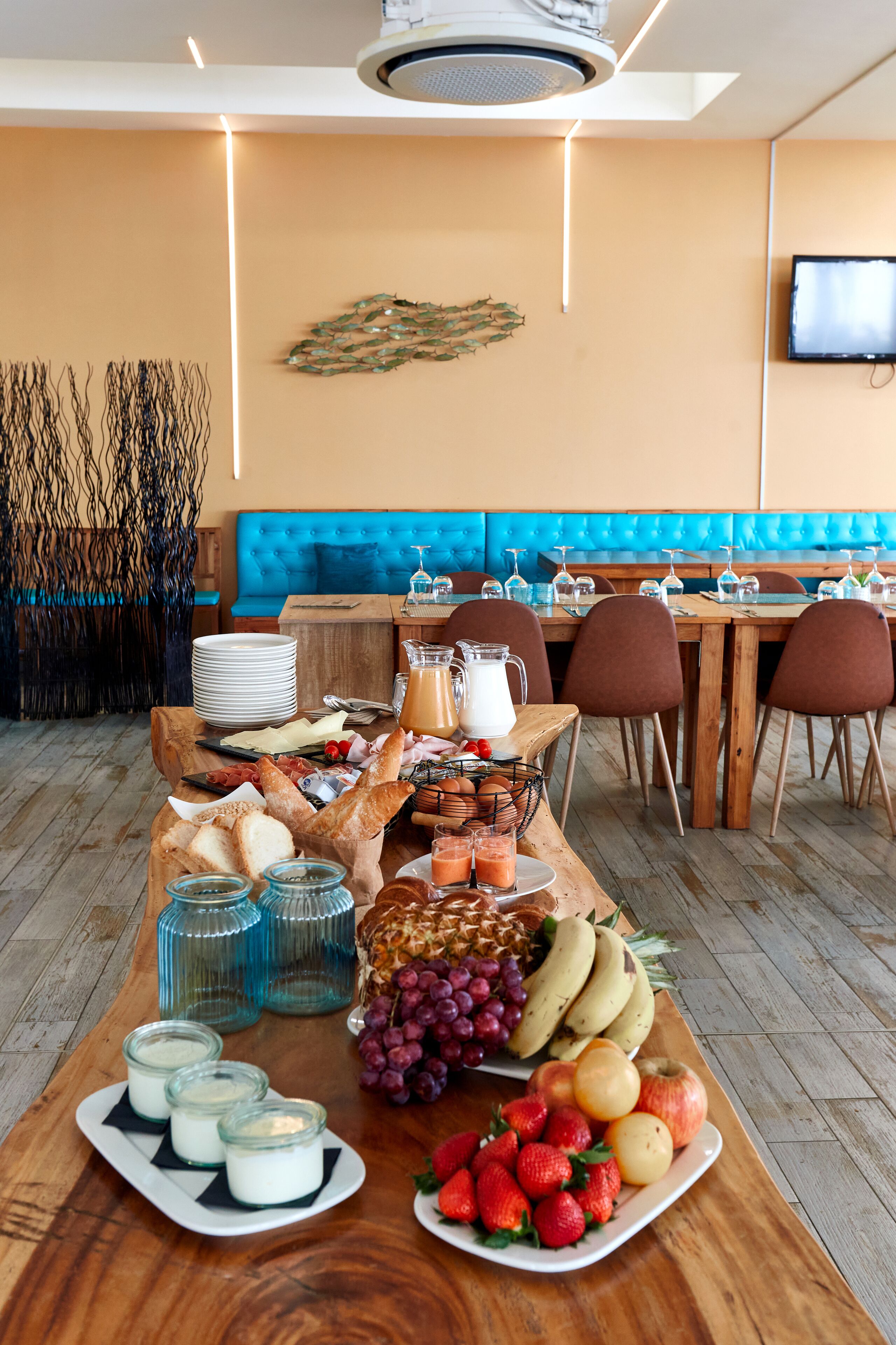 Un bufé de desayuno con diversos alimentos y un área de descanso con un sofá tapizado en azul y mesas de madera.