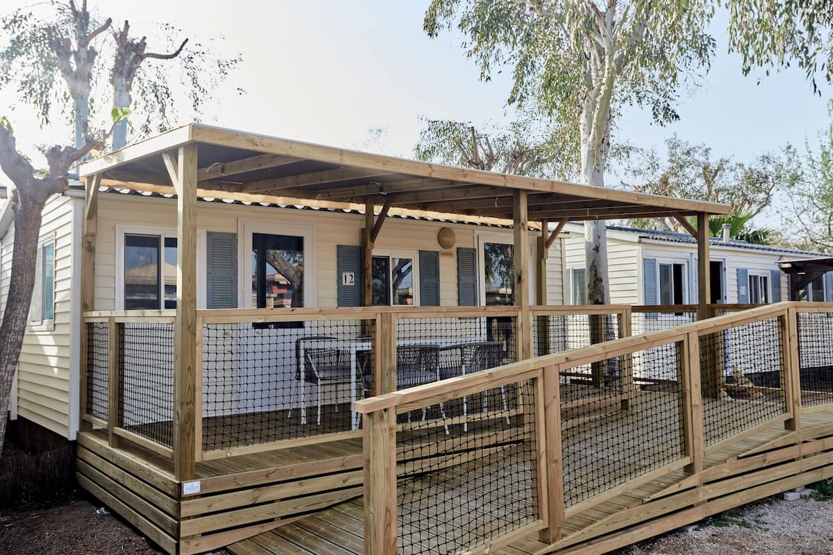 Eine Holzterrasse mit überdachtem Patio, umgeben von einem Holzzaun und einem Maschendrahtzaun.