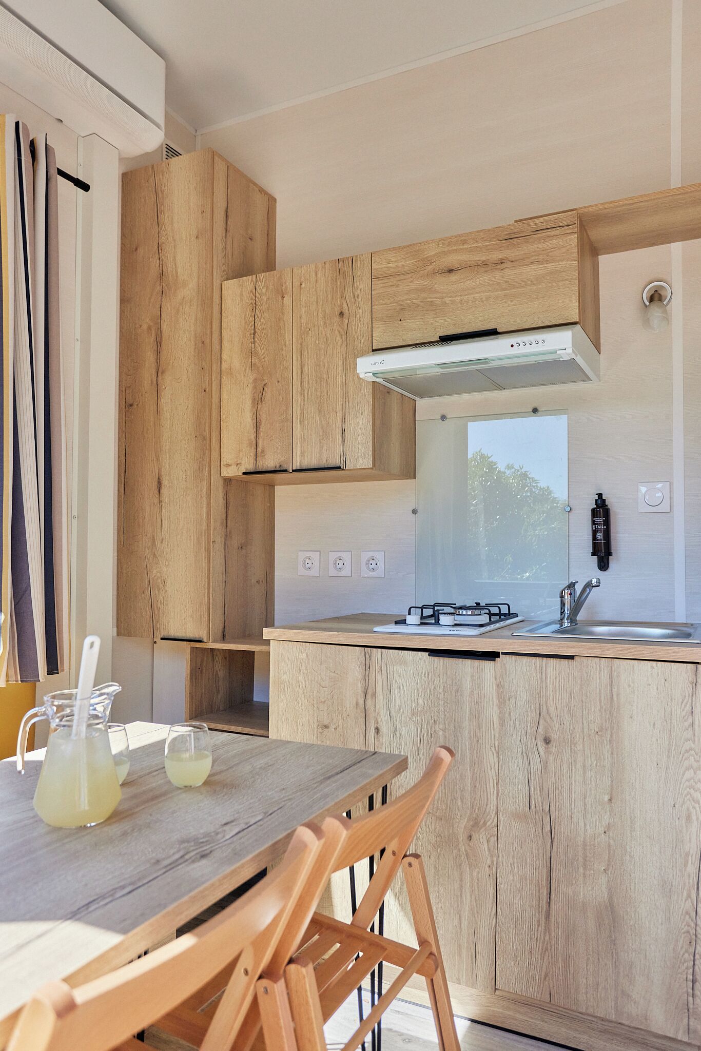 Een moderne keuken met houten keukenkastjes, een roestvrijstalen spoelbak en een eethoek met een houten tafel en stoelen.