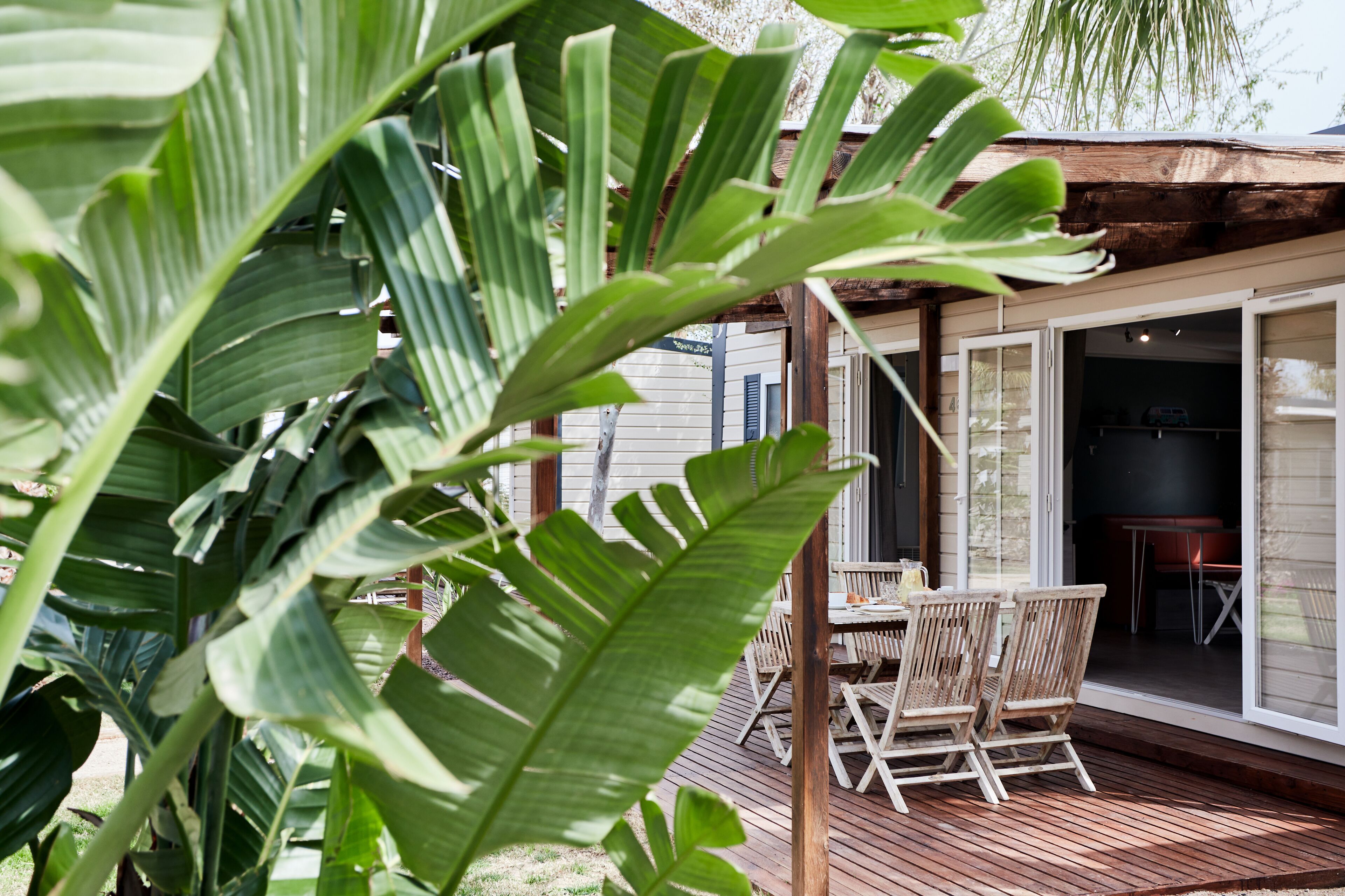 A wooden deck with outdoor furniture, a covered patio area, and a view of the house's interior through glass doors.