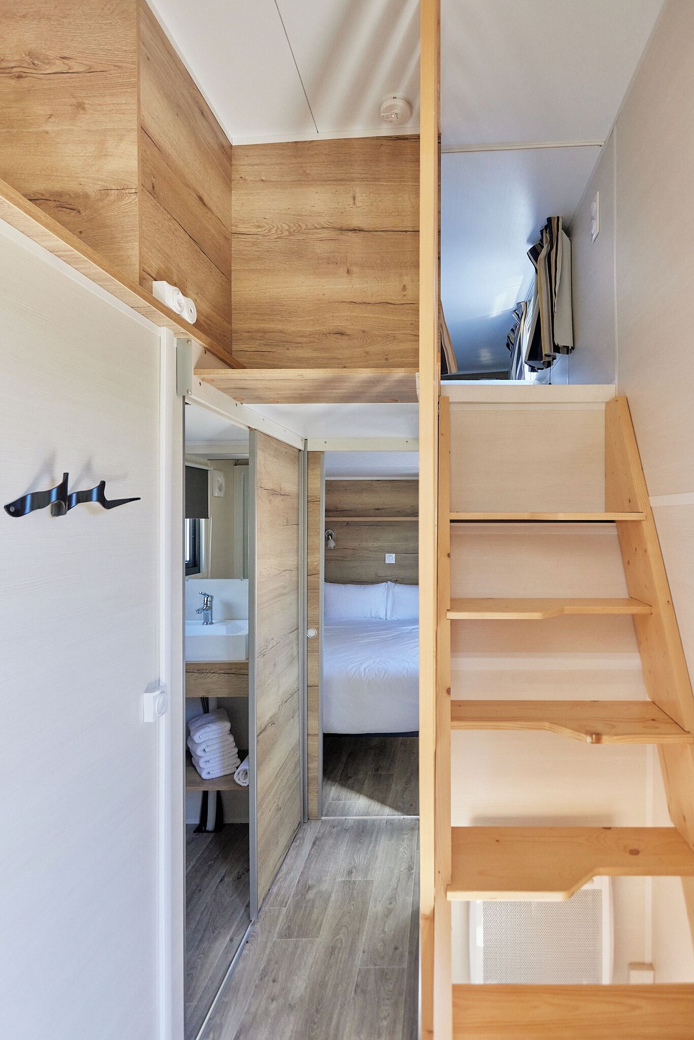A modern interior with a wooden staircase, a bathroom with a sink, and a wardrobe with a mirror.