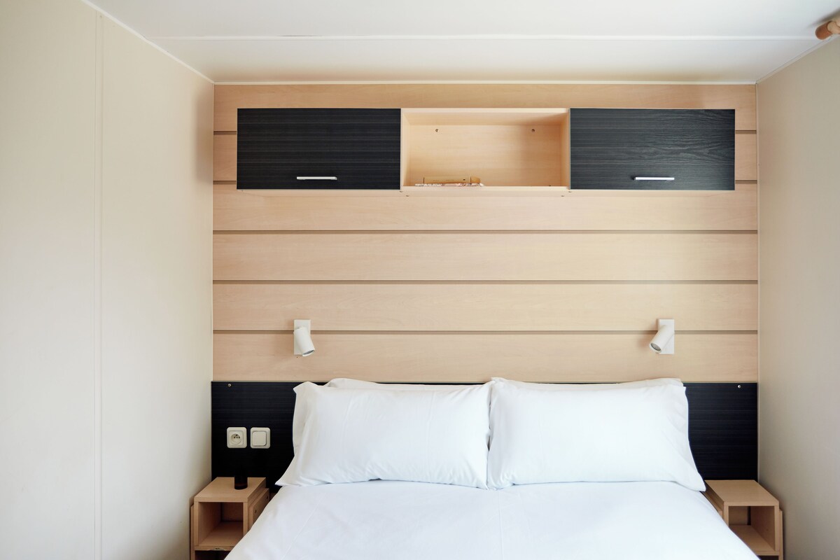 Una habitación de hotel moderna con un cabecero de madera, dos mesitas de noche y una cama con ropa de cama blanca.