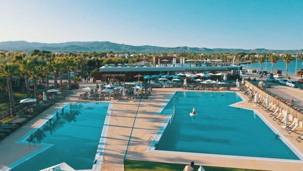 Un resort con dos piscinas amplias, tumbonas, sombrillas y vistas a las montañas.