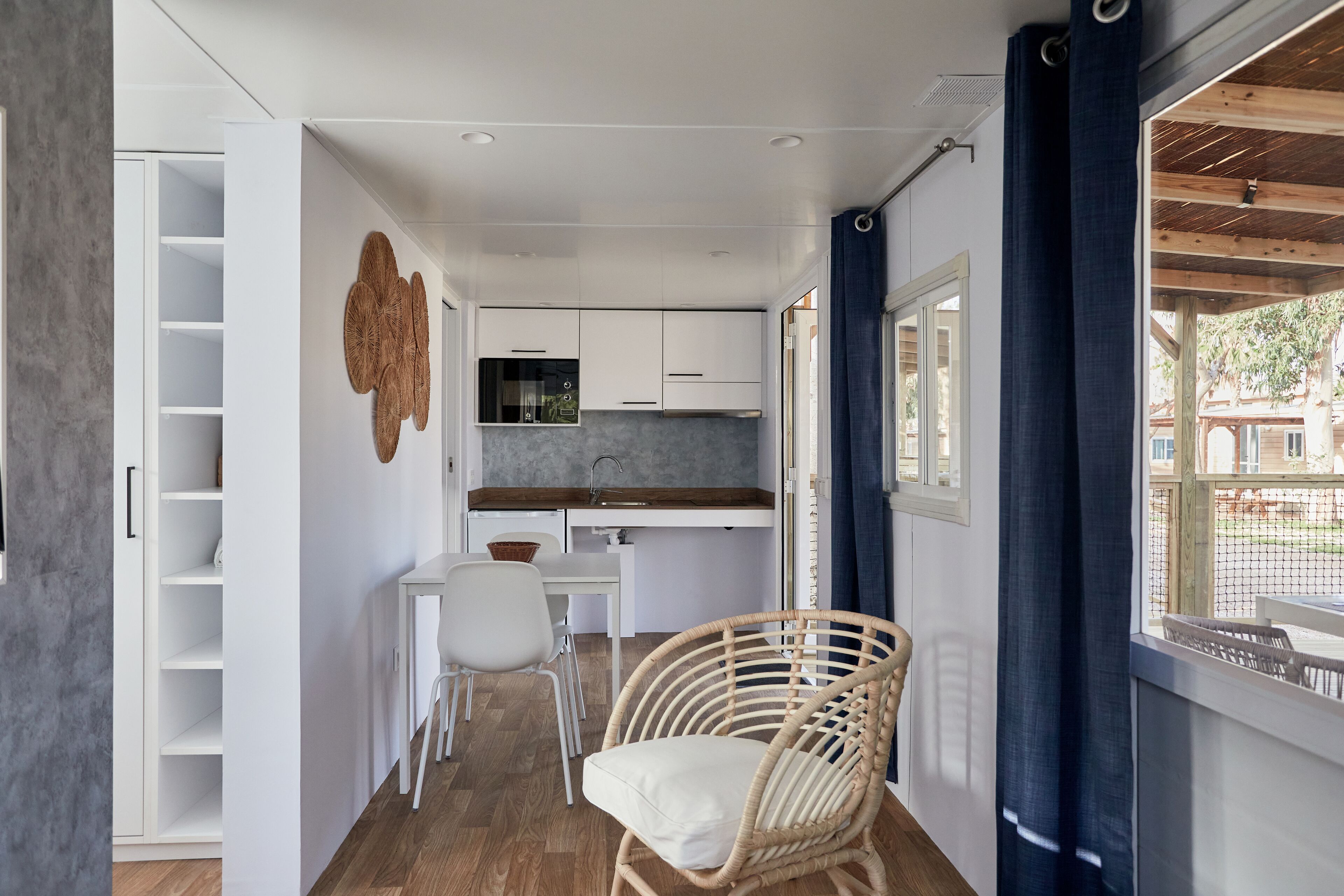 A compact kitchen with white cabinets, a dining table, and a wicker chair.