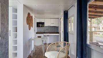 A compact kitchen with white cabinets, a dining table, and a wicker chair.