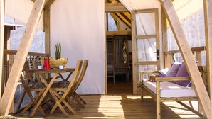 Una terraza de madera con una mesa, sillas y una cama con almohadones.