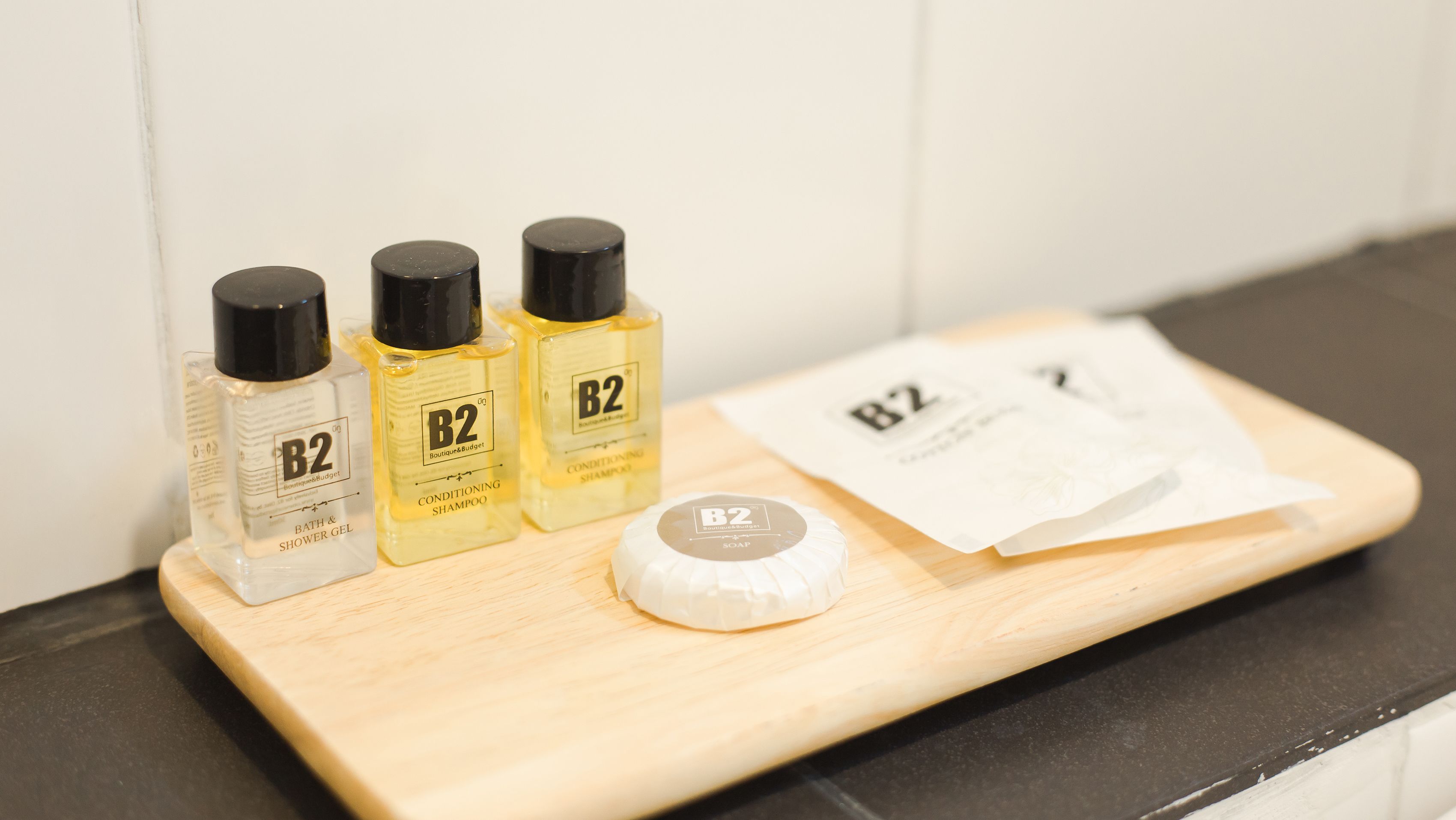 Three bottles of B2 conditioning shampoo, a bar of B2 soap, and a bar of B2 shower gel on a wooden tray.