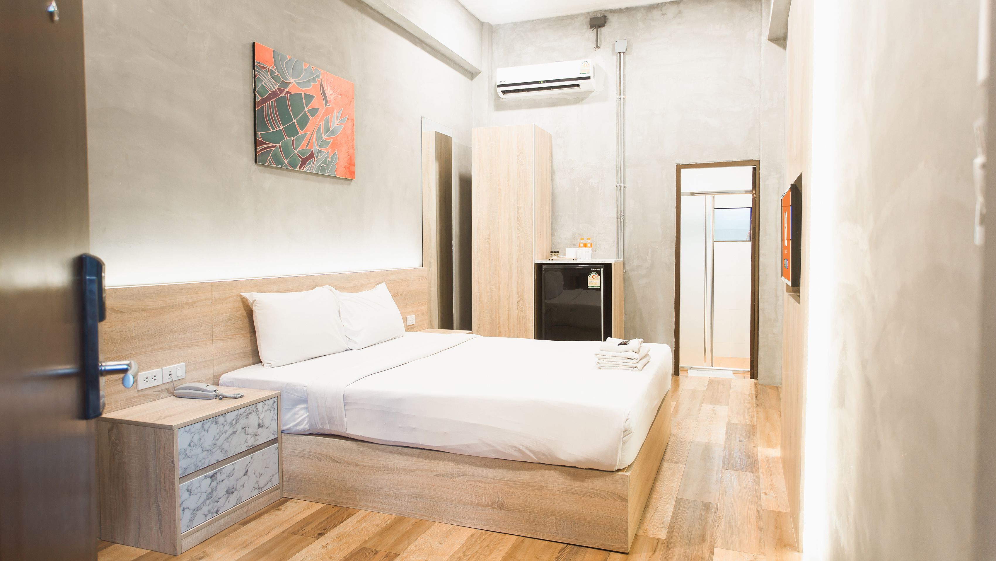 A modern hotel room with a wooden bed, a marble nightstand, a small desk, and an air conditioning unit on the wall.