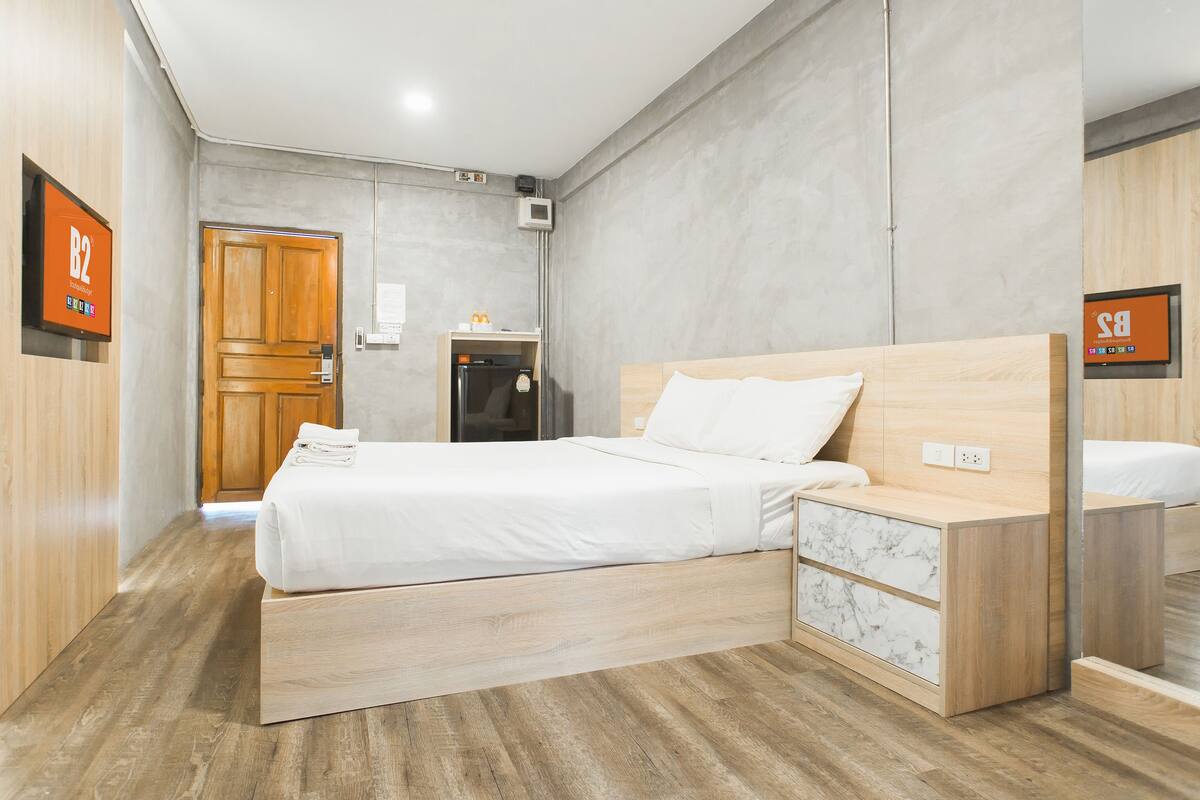 A modern hotel room with a wooden bed, a small bedside table, a marble drawer, and a wooden wardrobe.