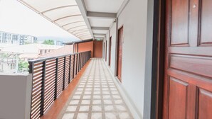 Um corredor com piso de azulejos, porta de madeira e corrimão de metal.