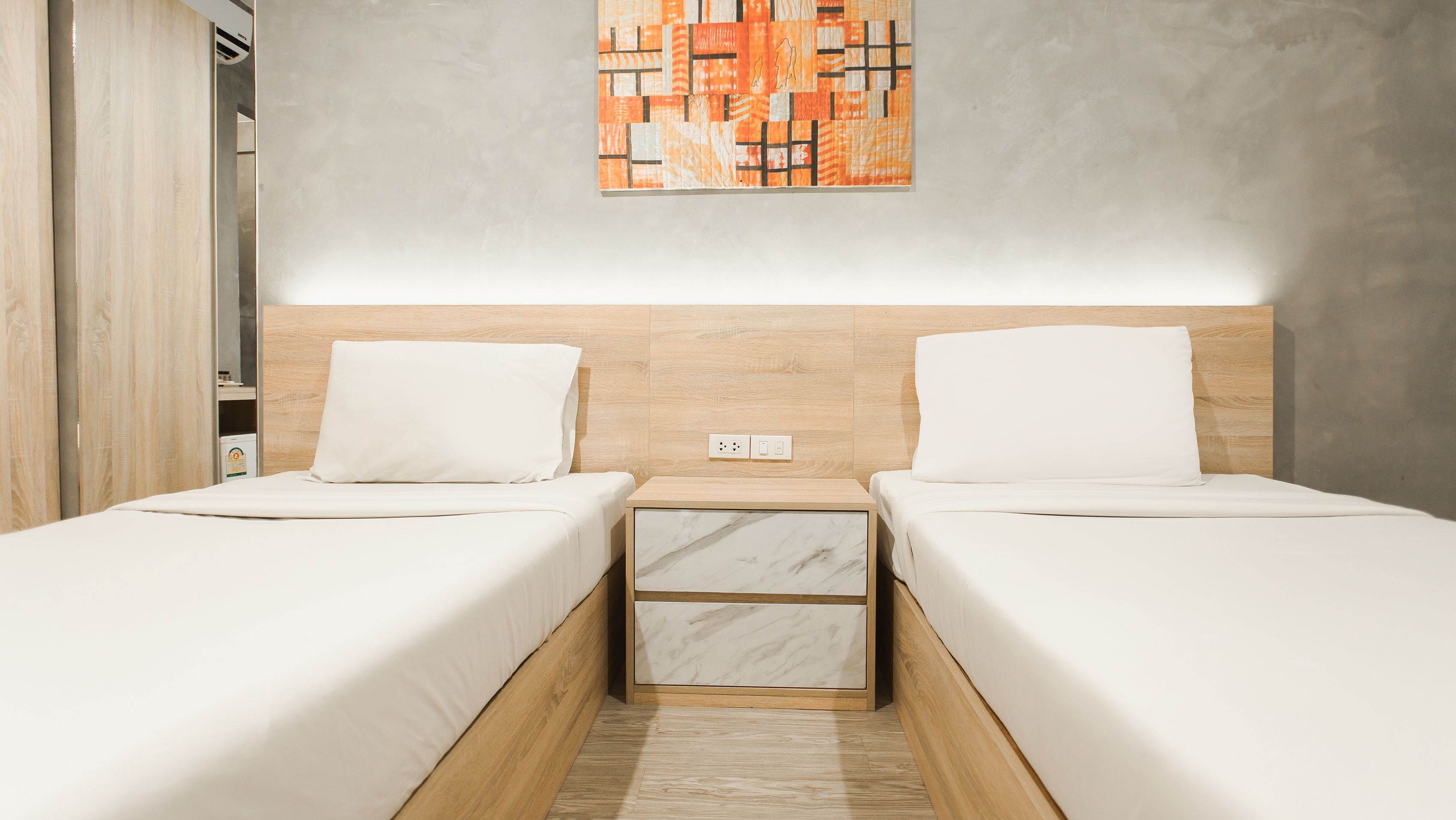 A modern hotel room with two single beds, a marble nightstand, and a wooden headboard.