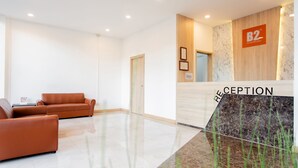 Uma área de recepção com um balcão de mármore, uma parede de madeira com uma placa, um sofá de couro marrom e uma porta.