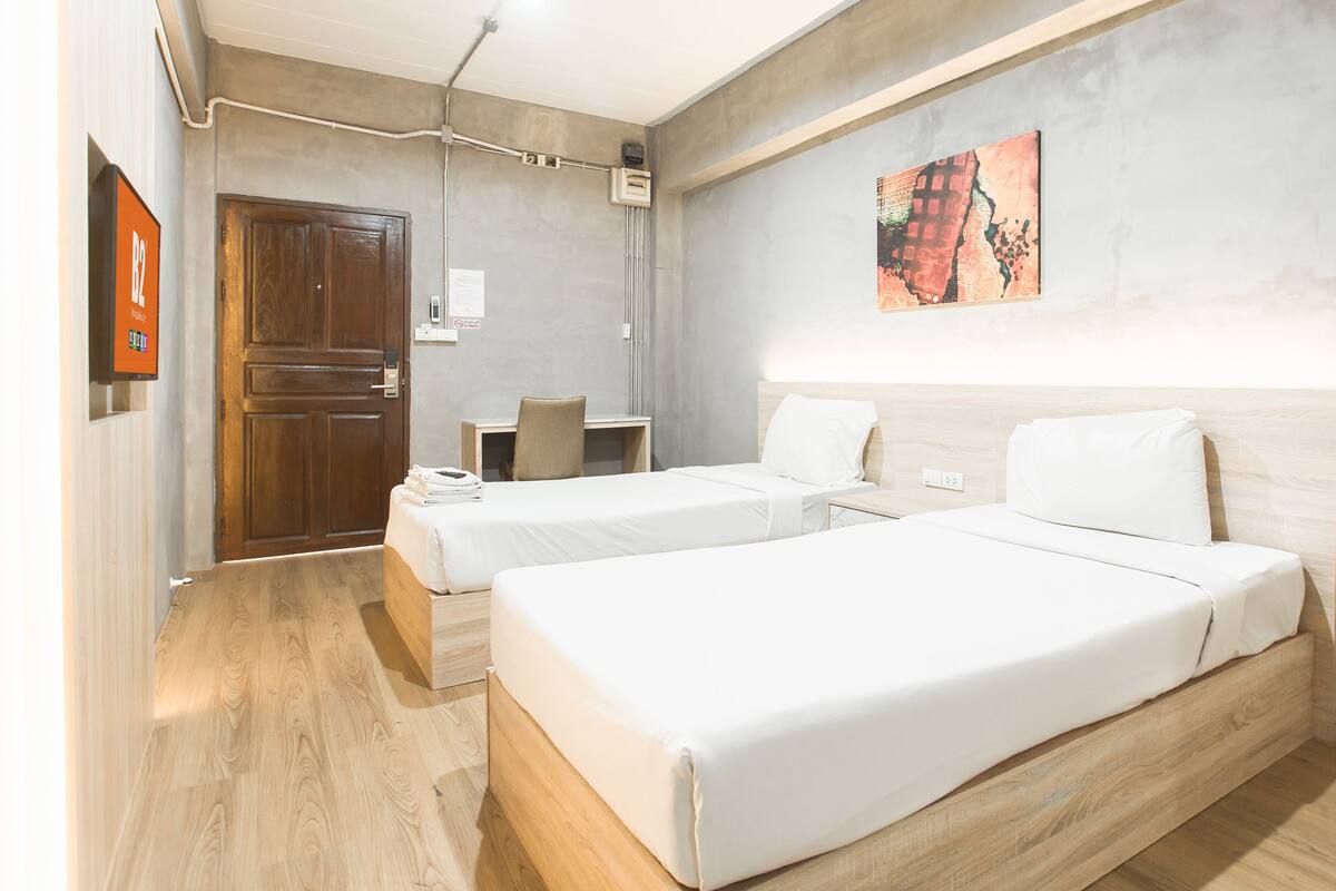 A hotel room with two beds, a desk, a chair, and a painting on the wall.