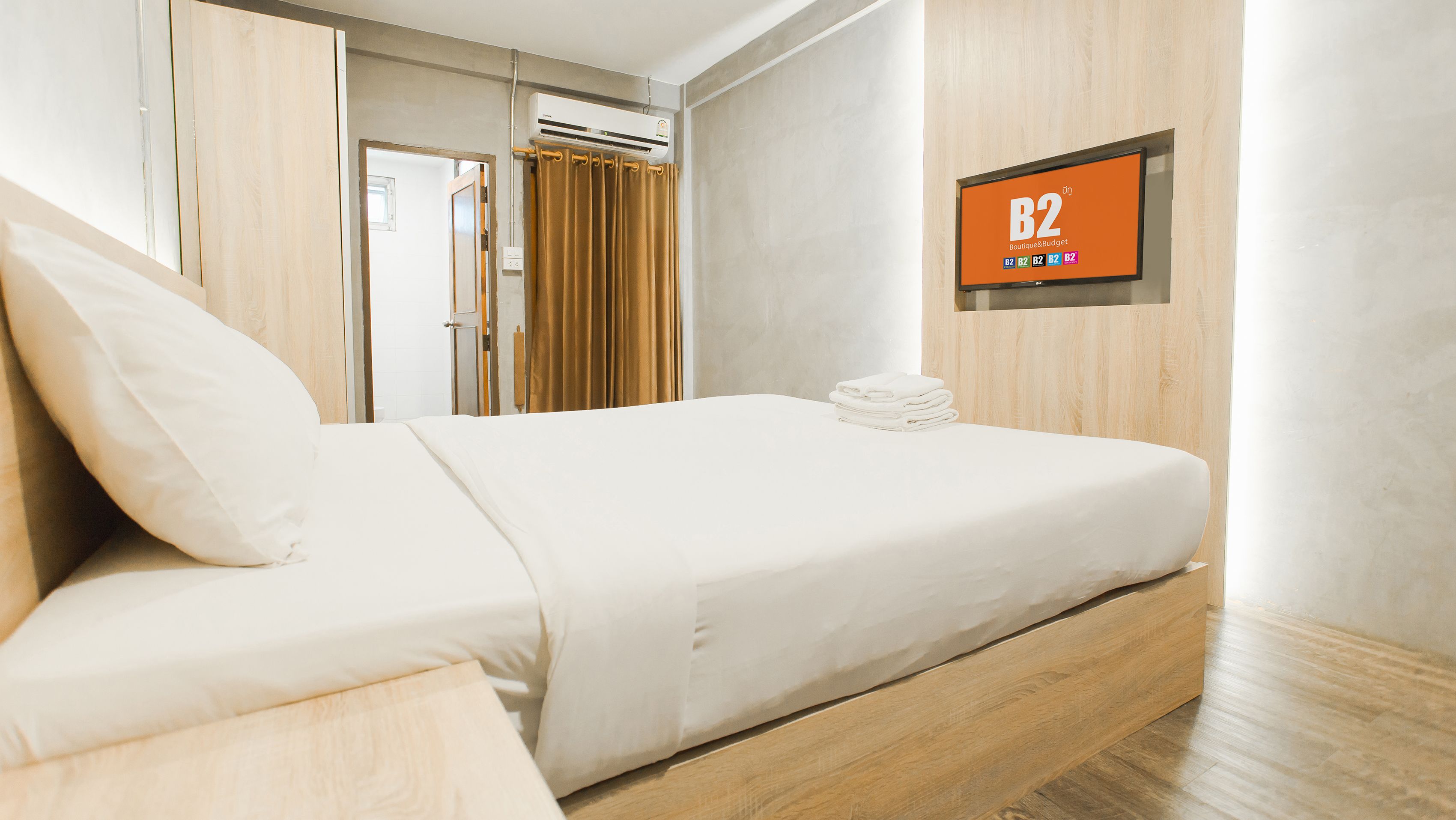 Ein Hotelzimmer mit einem Bett, einem Fernseher, der 'B2 Boutique & Budget' zeigt, und einem Holzschrank.