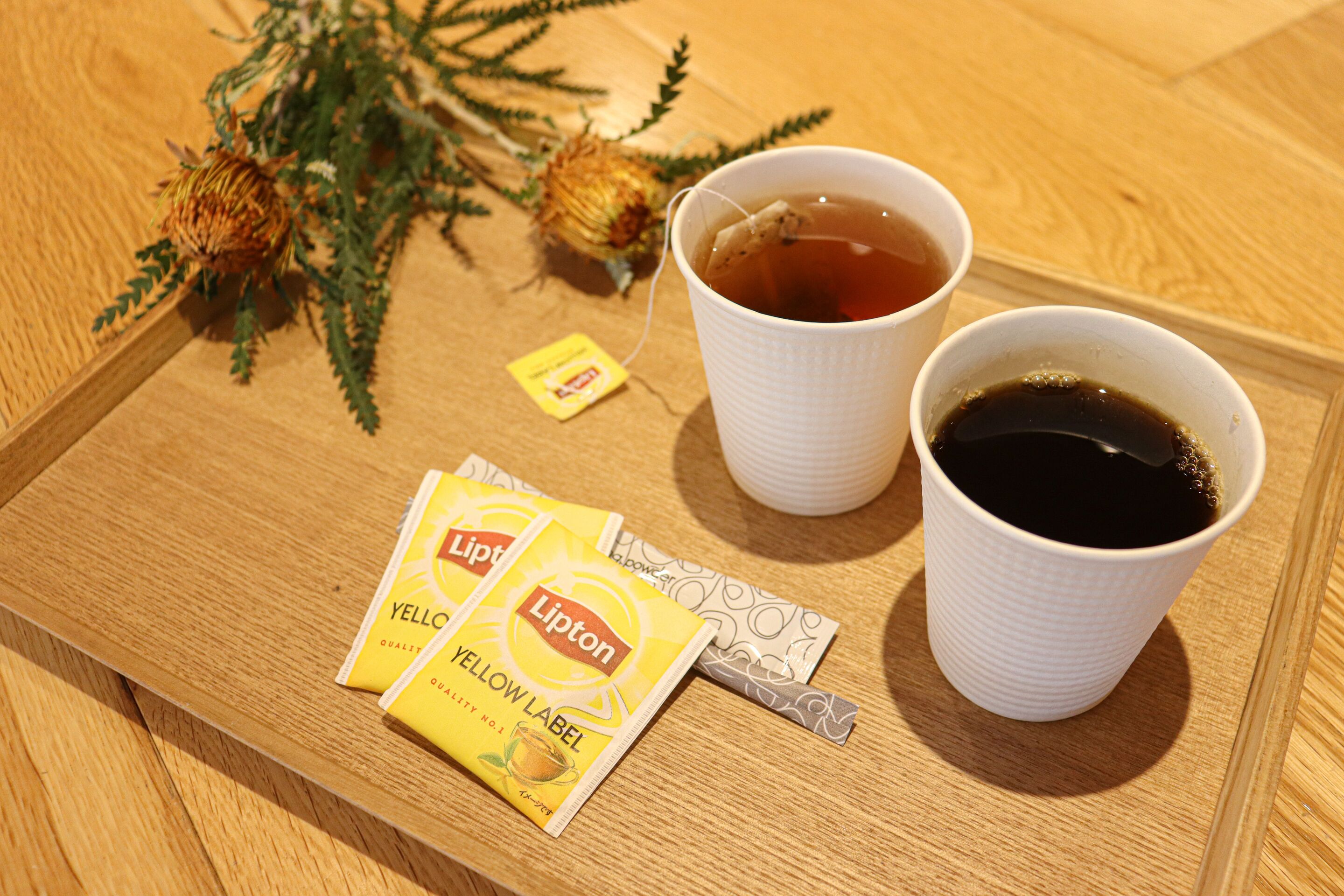 A tray with Lipton Yellow Label tea bags, a cup of tea, and a cup of black coffee on a wooden table.