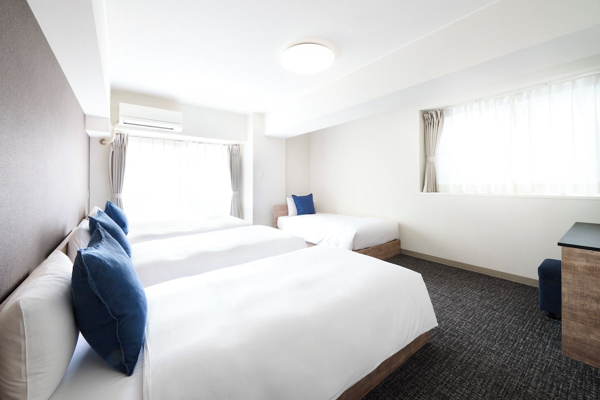 A hotel room with two beds, a desk, and a window with curtains.