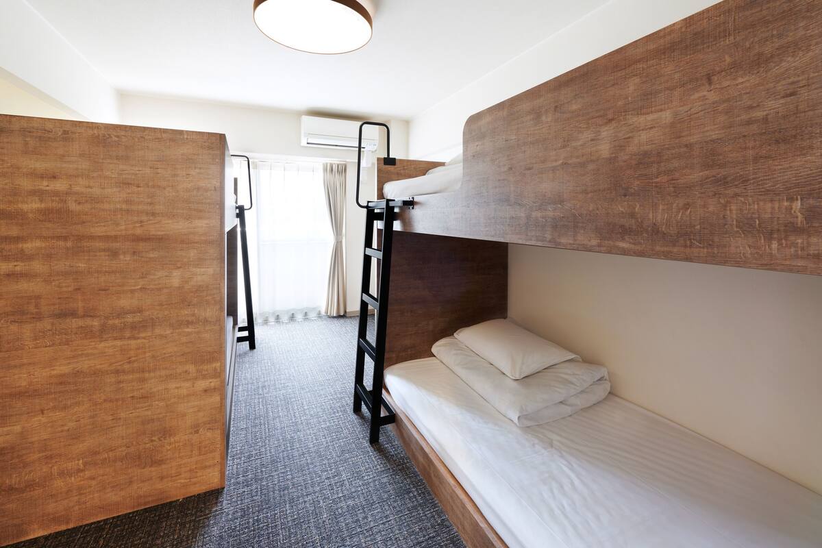 A bunk bed room with a ladder, a wardrobe, and a window with curtains.