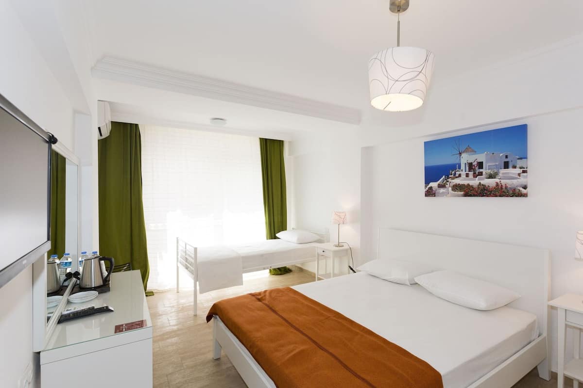 A hotel room with a bed, a desk, a chair, a lamp, a picture on the wall, and a window with curtains.