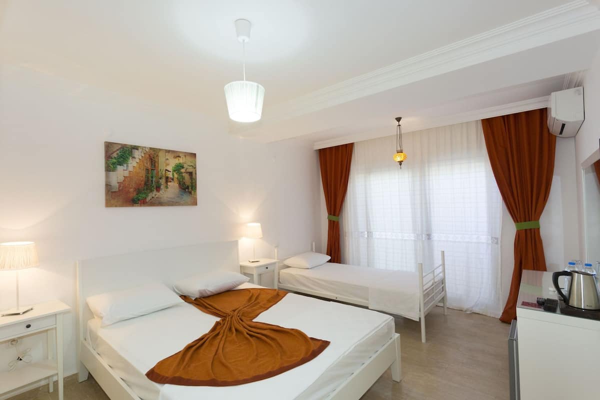 A hotel room with two beds, a painting on the wall, a window with curtains, a bedside table with a lamp, and a coffee maker on the dresser.