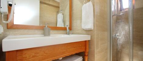 A bathroom with a wooden vanity, a white sink, a mirror, a towel rack, and a glass shower enclosure.